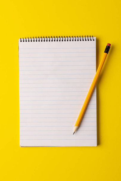 Vertical image of notebook with copy space and pencil on yellow surface. Business, working in office, equipment and tools concept. - Fotó, kép