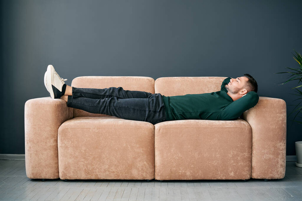 Young trendy man relaxing alone on textile sofa at home. Rest concept - Foto, Imagem