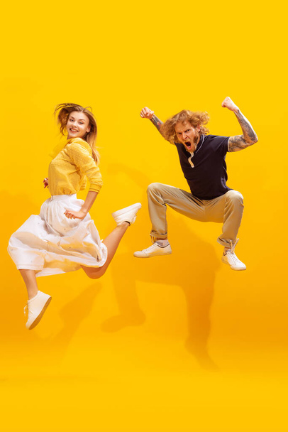 Portret van jonge man en vrouw in casual kleding poseren in een sprong geïsoleerd op gele studio achtergrond. Super opgewonden blik. Concept van jeugd, levensstijl, relatie, emoties, gezichtsuitdrukking, reclame - Foto, afbeelding