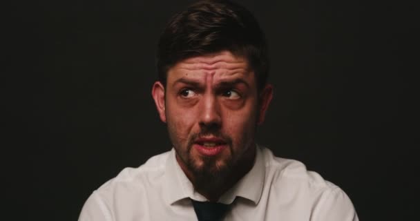 Nervous man looking worried and afraid against black studio background. A scared male suspect interrogated and looks around worryingly and being fidgety. Male under pressure and acting suspiciously. - Séquence, vidéo