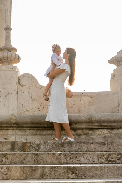 Веселая женщина держит дочь малыша на каменной лестнице моста Пуэнте-дель-Мар в Валенсии - Фото, изображение