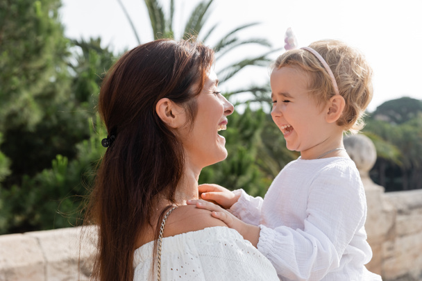Брюнетка мать держит дочку и смеется в Валенсии - Фото, изображение