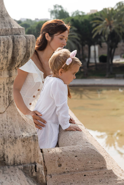 Side view of woman touching baby daughter on Puente Del Mar bridge above river in Valencia - Zdjęcie, obraz