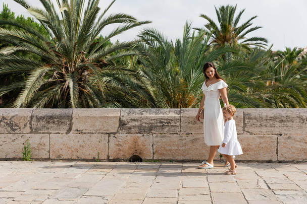 Woman and baby in summer dresses walking near palm trees in Valencia - Fotografie, Obrázek