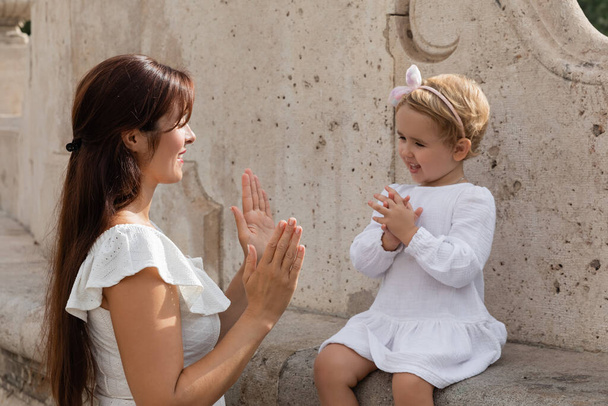 Brunette woman playing patty cake game with baby girl on stone bench in Valencia - Fotografie, Obrázek