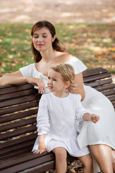 Toddler girl holding cookie near mom on bench in park  - Zdjęcie, obraz