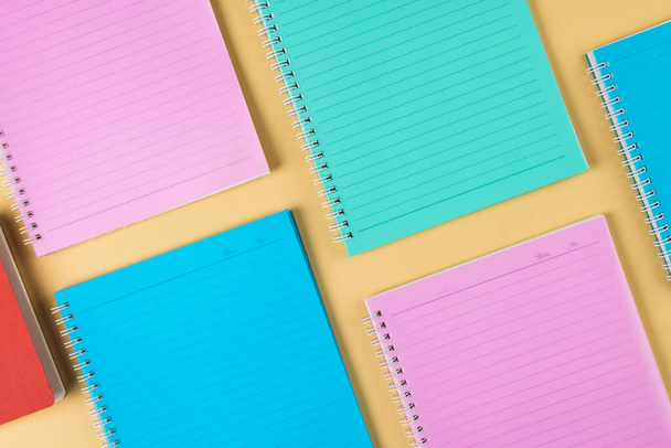 Composition of diverse colorful notebooks lying on yellow surface. School equipment, tools and creativity concept. - Photo, Image