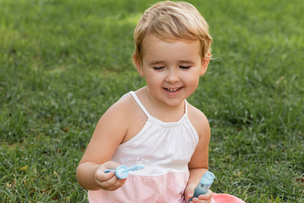 Positive toddler kid playing with soap bubbles on grass in park  - 写真・画像