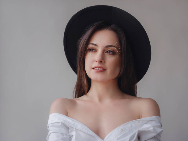 Schoonheid, mode studio portret van jonge vrouw met parel make-up in zwarte hoed geïsoleerd op witte achtergrond. Esthetiek van minimalisme. Concept voor spa, trouwsalons, schoonheidsbehandelingen. - Foto, afbeelding