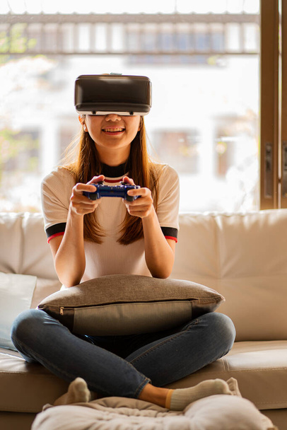 Приваблива жінка в гарнітурі VR жестикулює і посміхається, сидячи на дивані у вітальні вдома. відпочиває в окулярах віртуальної реальності, щоб грати в ігри
 - Фото, зображення