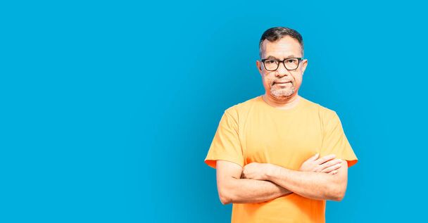 A man stood with his arms crossed. Wear an orange shirt and look at the camera. A man stood smiling happily after he retired. the concept for people, person, businessman. Copy space. Blue background - Foto, afbeelding