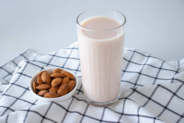 Almond milk in a glass with nuts on a white background and checkered napkin. - Fotoğraf, Görsel