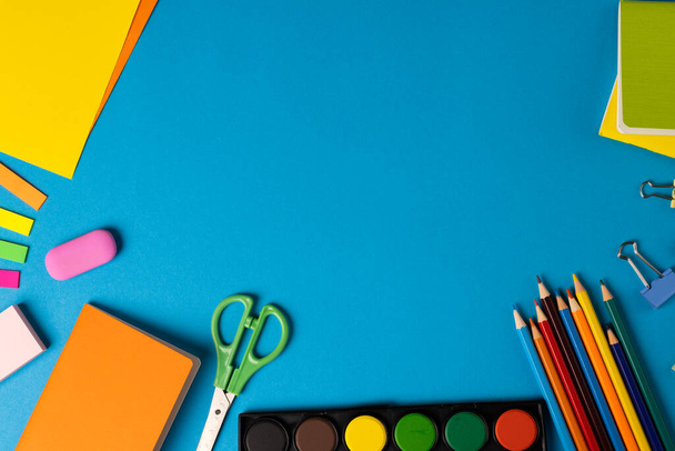Composition of colorful school items with scissors and empty cards on blue surface with copy space. School equipment, tools and creativity concept. - 写真・画像