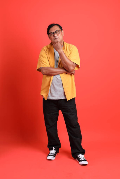 The adult Asian man with yellow shirt standing on the orange background. - Valokuva, kuva