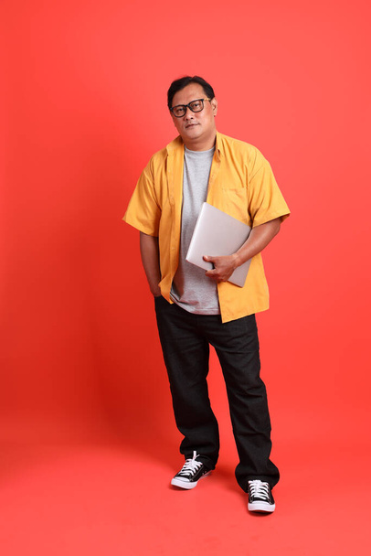 The adult Asian man with yellow shirt standing on the orange background. - Foto, Imagen