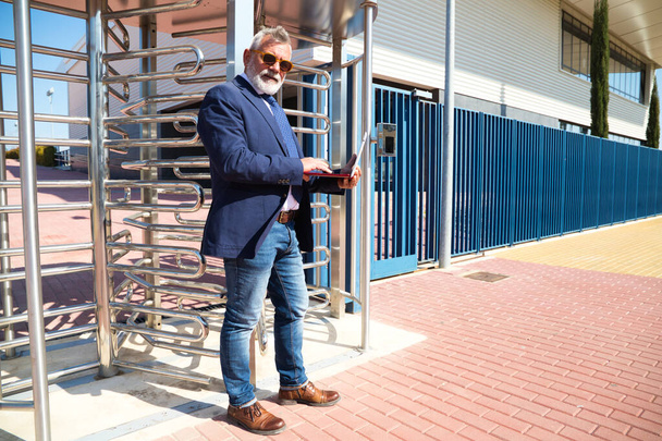 Mature professor, grey-haired, bearded, with sunglasses, is consulting his laptop before entering the university. Concept of education and teaching. Teachers and retirement. - Foto, Bild