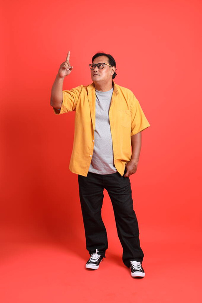 The adult Asian man with yellow shirt standing on the orange background. - Photo, Image