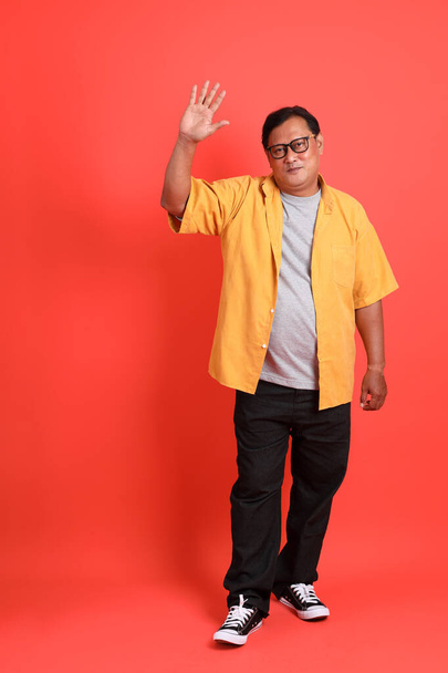 The adult Asian man with yellow shirt standing on the orange background. - Foto, Bild