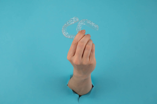 A female hand sticking out of a hole from a blue background holds removable night retainers - Foto, Imagem