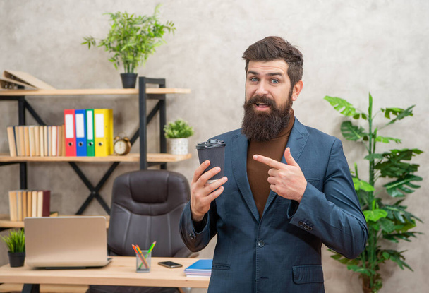 amazed bearded businessman pointing finger on takeaway coffee in the office with copy space, to go. - Foto, imagen
