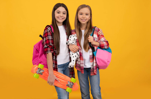学校に戻って。知識の日だ。教育の概念です。子供たちはスケートボードでヒップスター。9月1日幸せな子供時代。学校の袋を持った子供たち。明るいですティーン女の子運ぶバックパックおもちゃとペニーボード. - 写真・画像