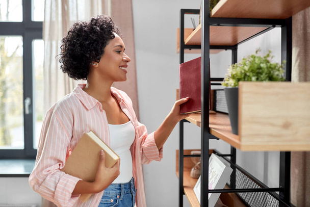 home improvement and people concept - happy smiling woman arranging books on shelving - Фото, изображение