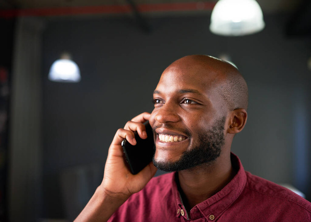 A Black man smiles on a cellphone call in the office. High quality photo - Zdjęcie, obraz
