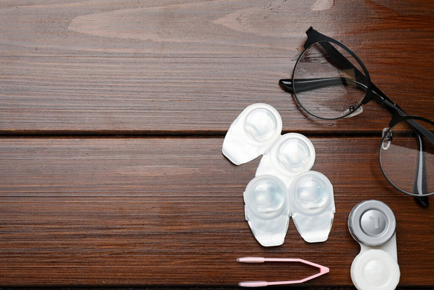 Packages with contact lenses, case, glasses and tweezers on wooden table, flat lay. Space for text - Fotografie, Obrázek
