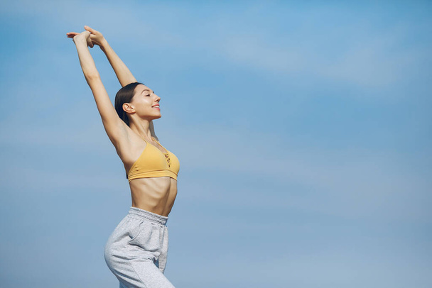 Beautiful girl training on a sky background. Woman in a yellow top. Lady make a yoga - Fotó, kép