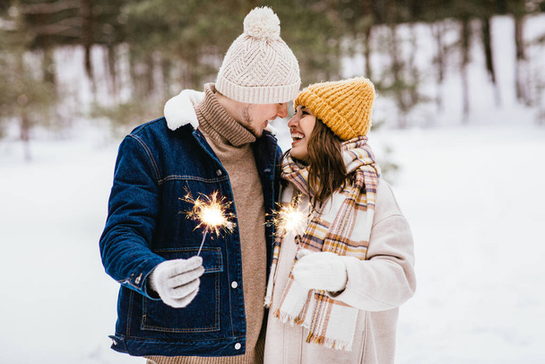 people, christmas and holidays concept - happy smiling couple with sparklers in winter forest - Fotó, kép