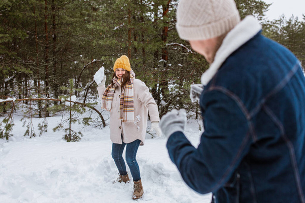 people, season and leisure concept - happy couple playing snowballs in winter park - Photo, Image