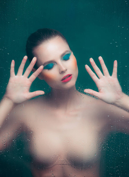 Yellow blush. Portrait of beautiful woman with bright makeup posing in underwear isolated over dark green background. Foggy glass effect. Concept of beauty, fashion, style, cosmetology, cosmetics. - Φωτογραφία, εικόνα