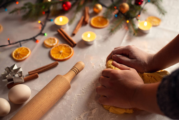 Le mani di una donna che fa la pasta per biscotti, pan di zenzero, biscotti in cucina. Diverse decorazioni natalizie sul tavolo - Foto, immagini