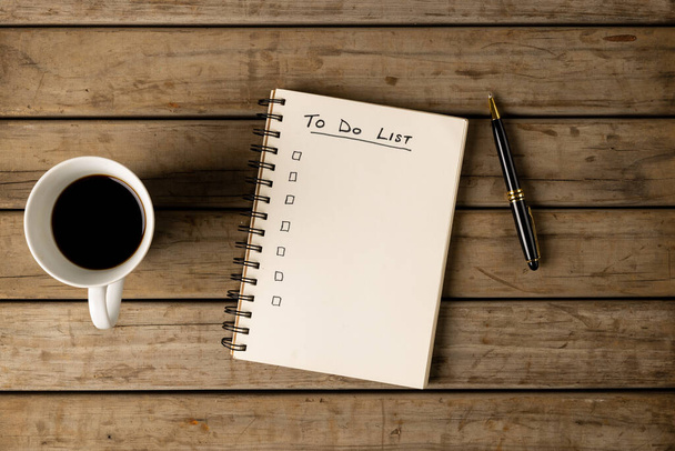 Image of notebook with to do list and copy space on wooden surface with coffee and pen. Business, tasks, office equipment and making notes concept. - Photo, image