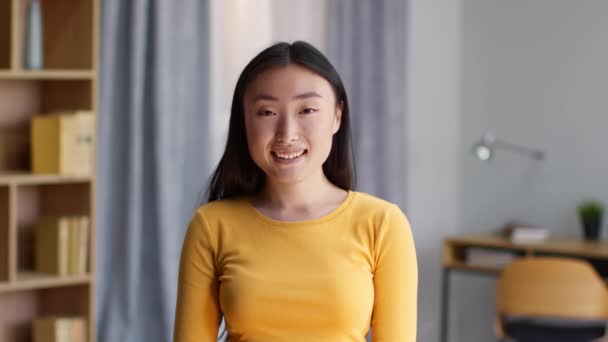 Youth and everyday lifestyle. Close up portrait of young happy asian woman smiling to camera, posing at domestic interior, slow motion - Imágenes, Vídeo