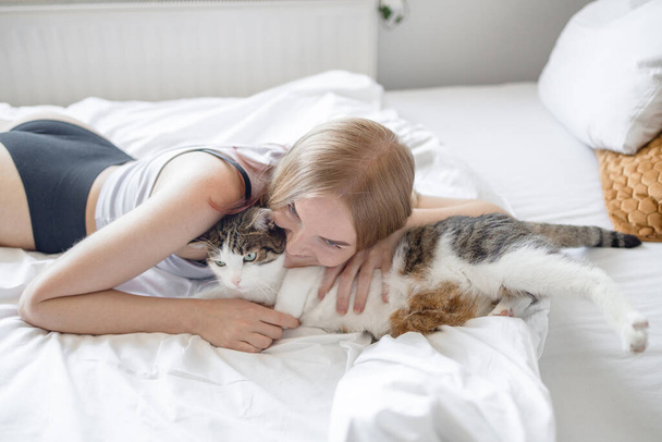 Vrouwelijke knuffelen droevige vermoeide kat in handen thuis. Blijf thuis. Blijf veilig. Liefde, zorg, adoptie - Foto, afbeelding