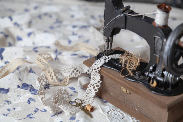 Vintage manual sewing machine and a skein of thread on a white fabric background with a blue pattern close-up. Braid and scissors lie nearb - Fotó, kép