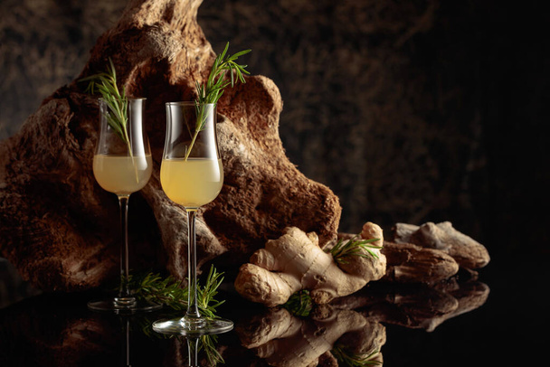 Ginger liquor with a rosemary branch on a black background with an old snag. - Foto, imagen