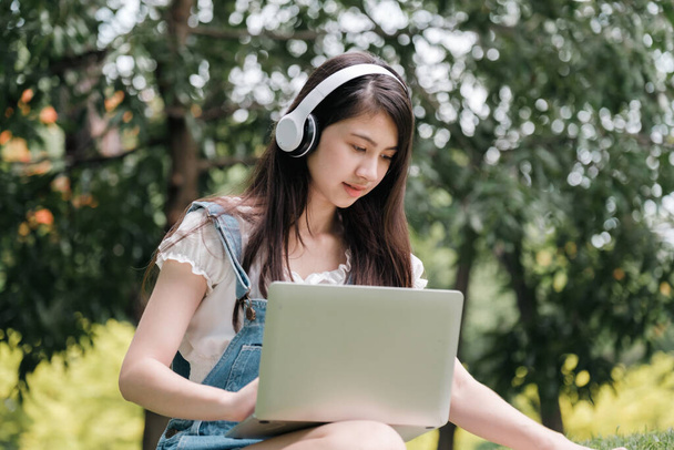 Young Asian teenage girl learning online with tablet and notebook in park. - 写真・画像