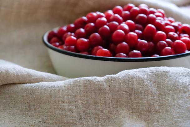 A metal bowl with cherries on a hemp tablecloth in natural light. Focus on the canvas. - Fotó, kép
