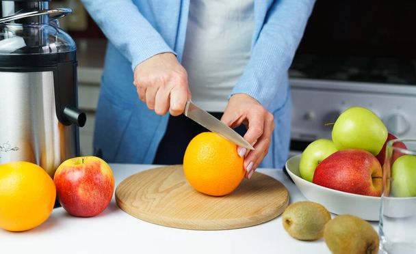 Young woman cuts an ripe orange for making fresh juice in the kitchen at home. Healthy food concept. Close-up. - 写真・画像