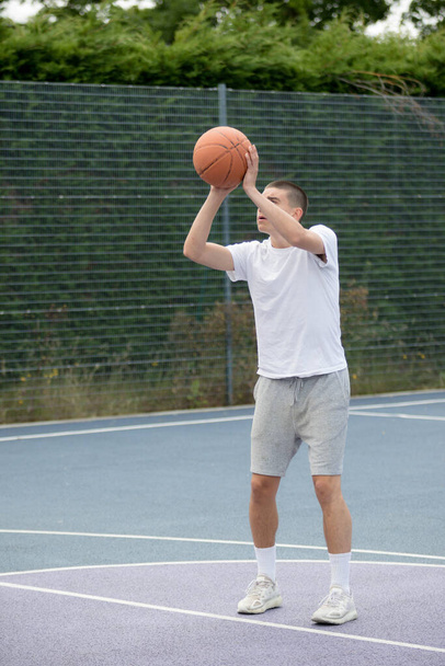 A Nineteen Year Old Teenage Boy Shooting A Hoop in A Basketball Court in A Public Park - Фото, изображение