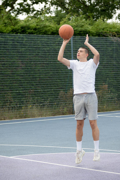A Nineteen Year Old Teenage Boy Shooting A Hoop in A Basketball Court in A Public Park - Фото, изображение