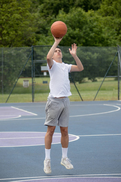 Dziewiętnastoletni nastolatek strzelający obręczą na boisku do koszykówki w parku publicznym - Zdjęcie, obraz