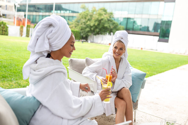 Happy young beautiful women enjoying fun time after spa procedures together in luxury hotel, wearing towels on heads and bathrobes. - 写真・画像