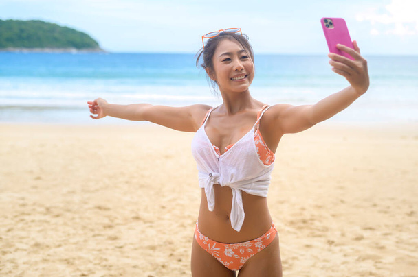 Young Beautiful woman in Bikini listening to music and using smartphone on the beach,  Summer, vacation, holidays, Lifestyles concept. - 写真・画像