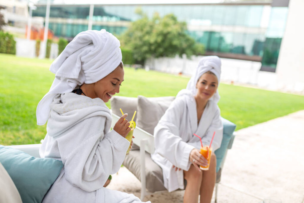 Happy young beautiful women enjoying fun time after spa procedures together in luxury hotel, wearing towels on heads and bathrobes. - Photo, Image