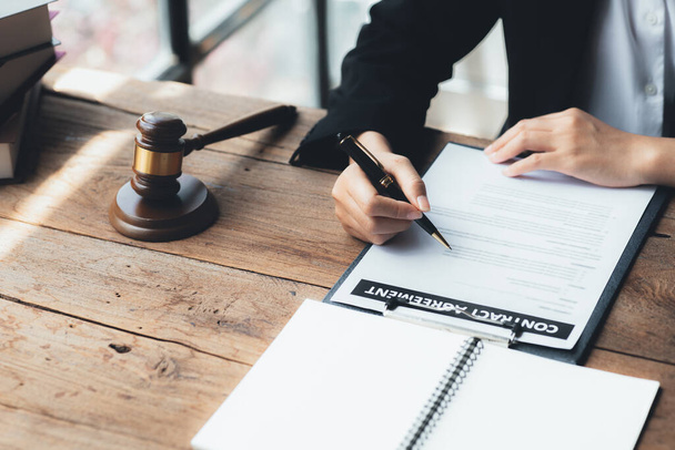 A lawyer sits in his office, on a table with a small hammer to beat the judges desk in court. and justice scales, lawyers are drafting a contract for the client to use with the defendant to sign. - Foto, Imagem