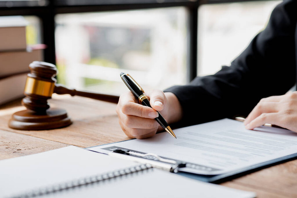 A lawyer sits in his office, on a table with a small hammer to beat the judges desk in court. and justice scales, lawyers are drafting a contract for the client to use with the defendant to sign. - Photo, image