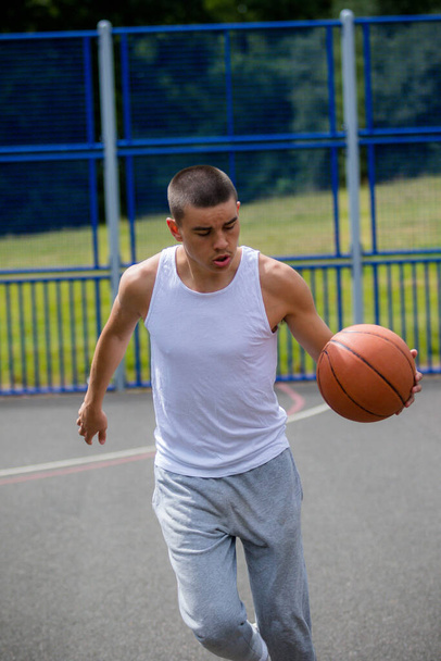 Un adolescente diciannovenne che gioca a basket in un parco pubblico - Foto, immagini